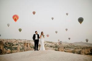 Bride and Groom on a mountain with hot air ballons showing all around them.